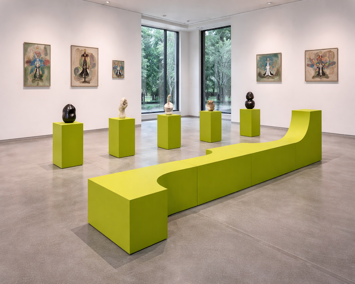 Modern art installation with sculptures on green pedestals in a gallery setting.